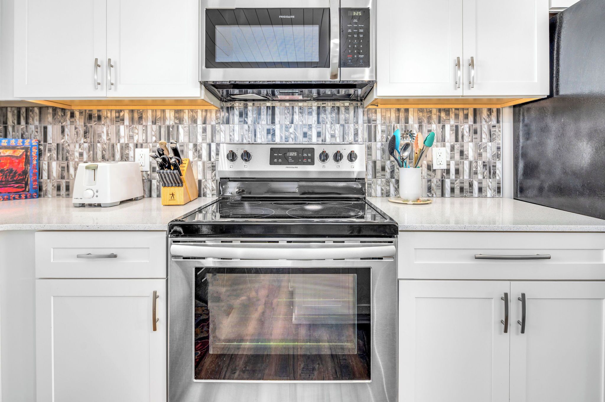 Una cocina moderna con armarios blancos, una estufa de acero inoxidable, un microondas y un tostador.