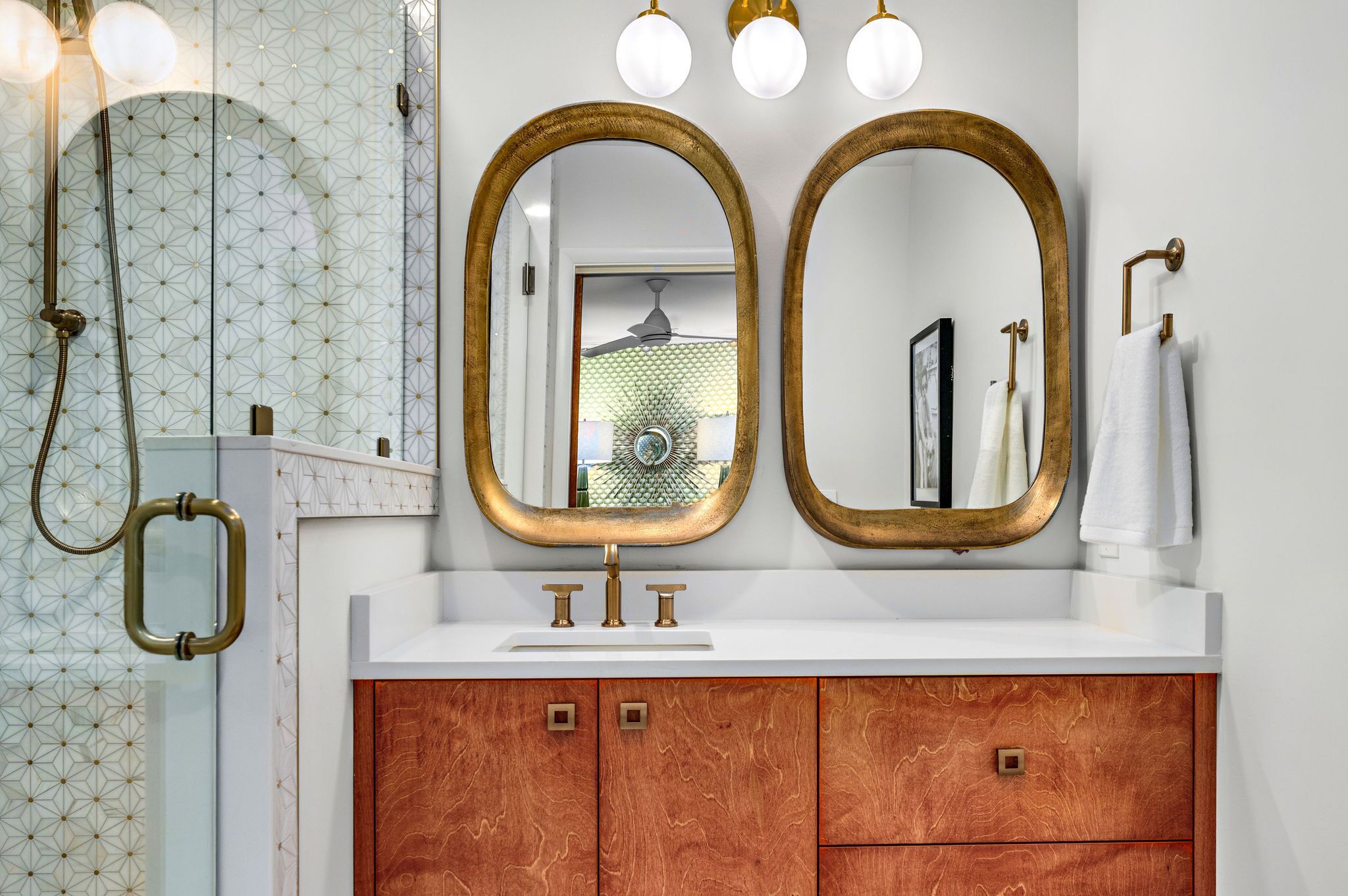 A bathroom with a white sink, two gold-framed mirrors, and a wooden vanity.