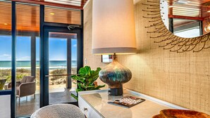 A modern interior with a large window offering a beach view, a round table with a lamp, and a wooden side table. - BEACHFRONT! PRIVATE POOL! All new renovation. (St. George Island)