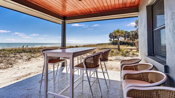 A covered outdoor seating area with a table and chairs, overlooking a beach and ocean. - BEACHFRONT! PRIVATE POOL! All new renovation. (St. George Island)