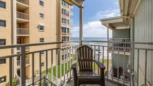 A balcony with a wooden chair, overlooking a building with multiple balconies and a view of the ocean.