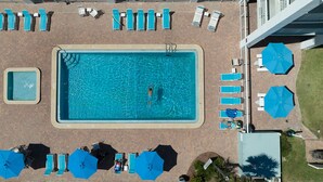 An aerial view of a rectangular swimming pool with a diving board, surrounded by lounge chairs and umbrellas.