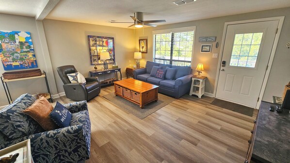 A living room with a dark leather armchair, a blue sofa, a wooden coffee table, and a ceiling fan. - Isle Be Back!: 3 BR, 2 BA Cottage in St. George Island, Sleeps 6 (St. George Island)