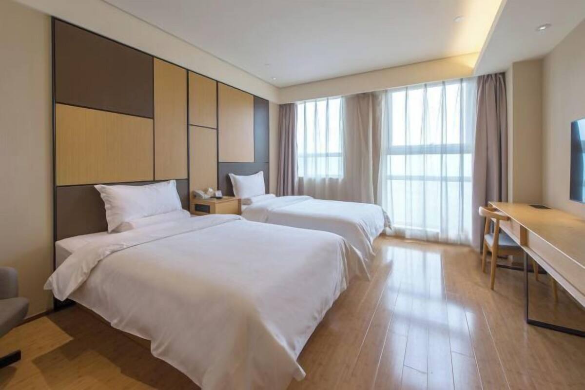 A hotel room with two beds, a desk, a TV, and large windows.