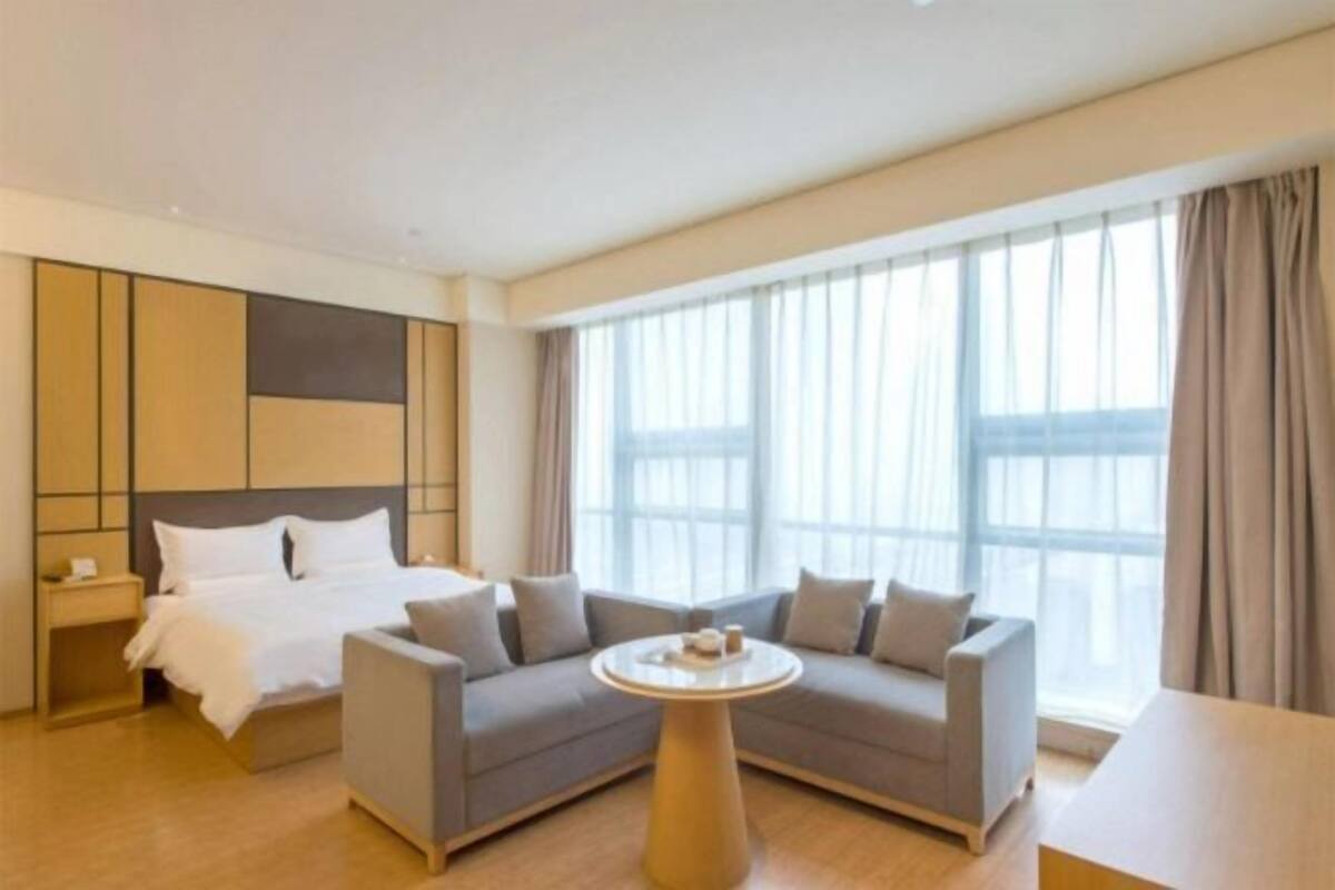A hotel room with a bed, a sofa, a round table, and large windows.
