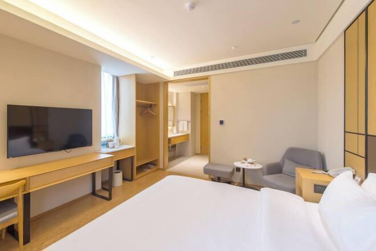 A hotel room with a bed, a TV, a desk, a chair, a small table, and a wardrobe.