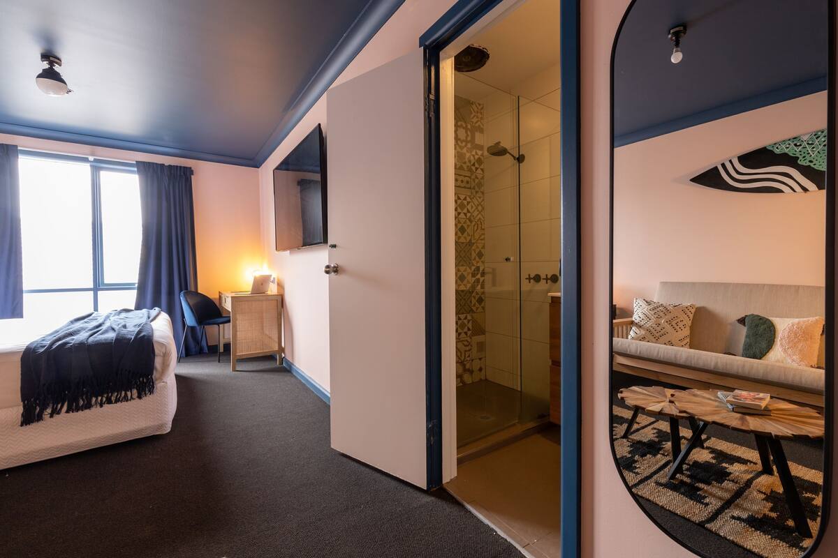 Habitación de hotel con cama, escritorio, sofá, ducha y espejo.