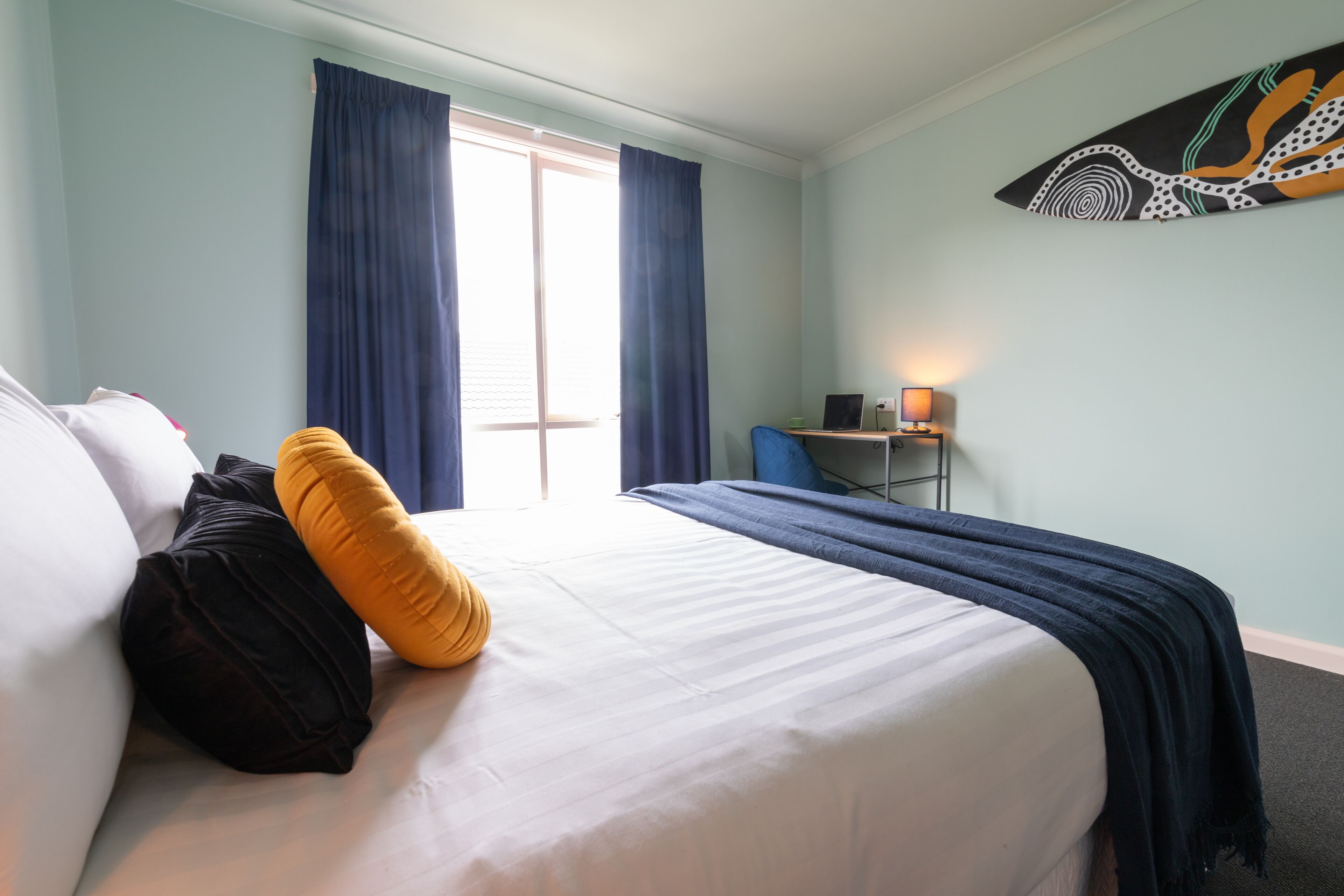A hotel room with a bed, a desk, a lamp, and a window with curtains.