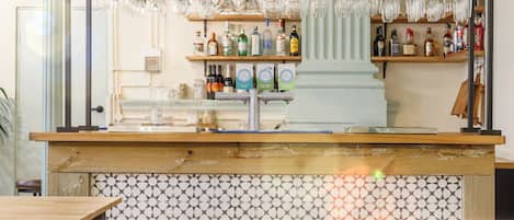 Una zona de bar con salpicadero de azulejos, taburetes de madera y una variedad de botellas y vasos en estantes.