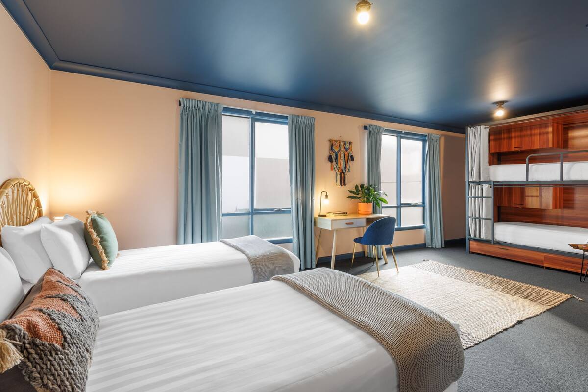 Habitación de hotel con dos camas, un escritorio, una silla y una litera.
