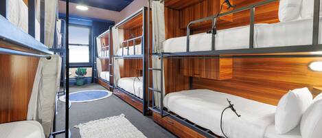 Quarto com beliches, ventoinha no teto e janela com cortinas.
