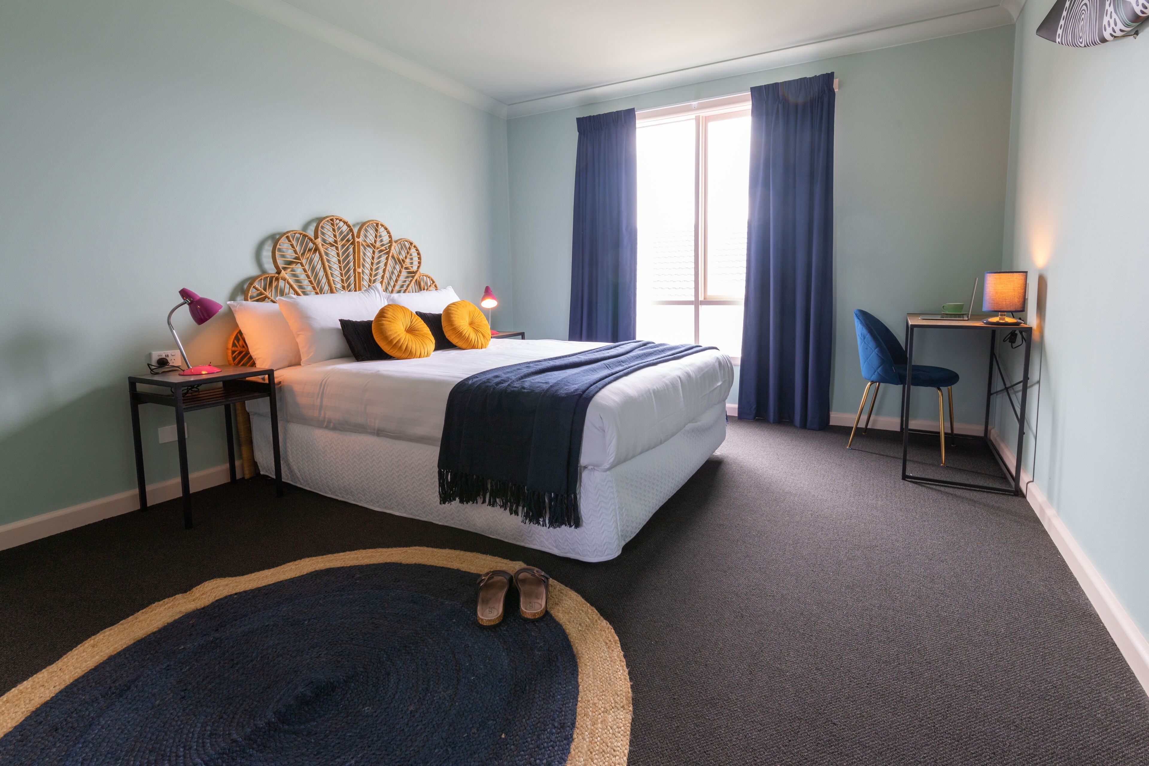 A bedroom with a bed, a desk, a chair, a laptop, and a window with curtains.