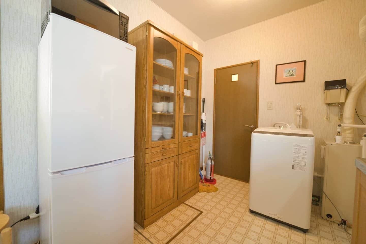 A compact kitchen with a white refrigerator, wooden cabinet with glass doors, and a white washing machine.