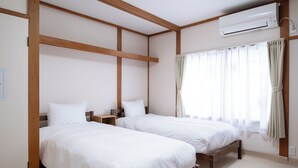 Una habitación con dos camas, vigas de madera, aire acondicionado y una ventana con cortinas.
