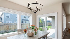 A dining area with a wooden table, chairs, and a chandelier. There are flower vases on the table.