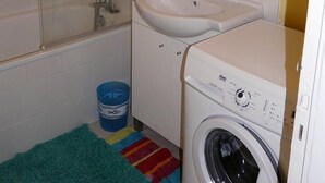 Un baño pequeño con ducha, lavabo y lavadora.