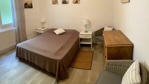 Habitación de hotel con cama, dos mesitas de noche, escritorio, silla, mesita de noche de madera y ventana con cortinas.