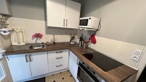 Una cocina compacta con armarios blancos, microondas, estufa y pileta.