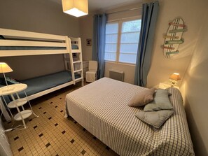 A room with bunk beds, a single bed, a small table, a chair, and a window with curtains.