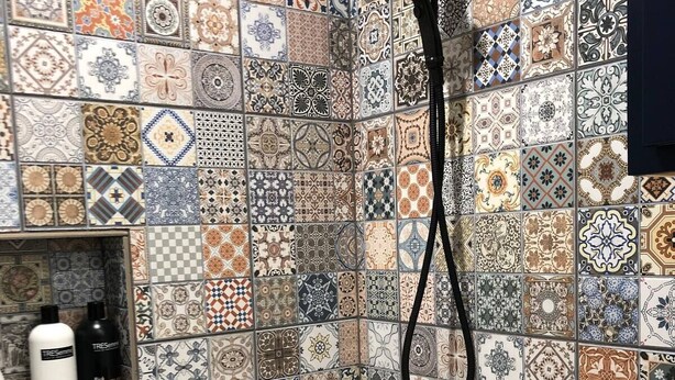 Een badkamer met een douche en wastafel, betegeld met verschillende patronen.
