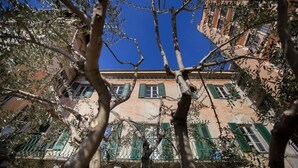 Un edificio de estilo arquitectónico tradicional, con un balcón con contraventanas verdes y suelo de baldosas.
