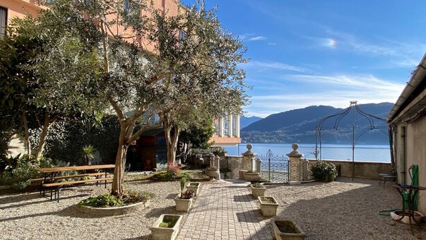 Un patio con un camino empedrado, bancos, plantas en macetas y vistas al mar y a las montañas.