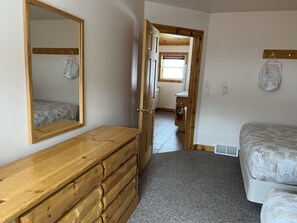 Ein Schlafzimmer mit einem Holzkapitänsbett, Bettwäsche mit Muster, einem Spiegel und einem Flur, der zu einem Badezimmer führt.