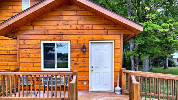 Una cabaña de madera con porche, puerta y ventana.