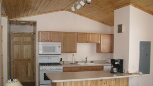 Una cocina con gabinetes de madera, microondas, estufa, fregadero y taburetes de bar.