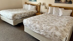 Una habitación de hotel con dos camas, un cabecero de madera, una mesita de noche con una lámpara y dos cuadros en la pared.