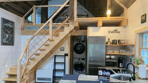 A modern kitchen with a wooden staircase, a built-in washing machine, and a stainless steel refrigerator. - Brand new cabin in the Adirondacks near Whiteface Mountain! (Wilmington)