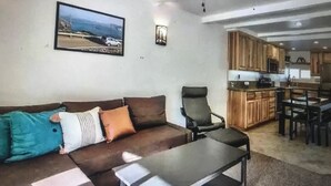 A living room with a sofa, armchairs, and a coffee table. There is a ceiling fan, a kitchen area with wooden cabinets, and a framed picture on the wall. - Boreal condo 3 bed 2 bath near Boreal, Soda Springs on Boreal Lake & near Donner (Truckee)