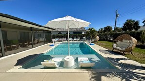A rectangular swimming pool with lounge chairs and a large umbrella. - Private Naples Oasis w/ Cart, Gym & Saltwater Pool (Naples)