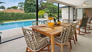 A dining area with a pool view, wicker chairs, and a wooden table. - Private Naples Oasis w/ Cart, Gym & Saltwater Pool (Naples)
