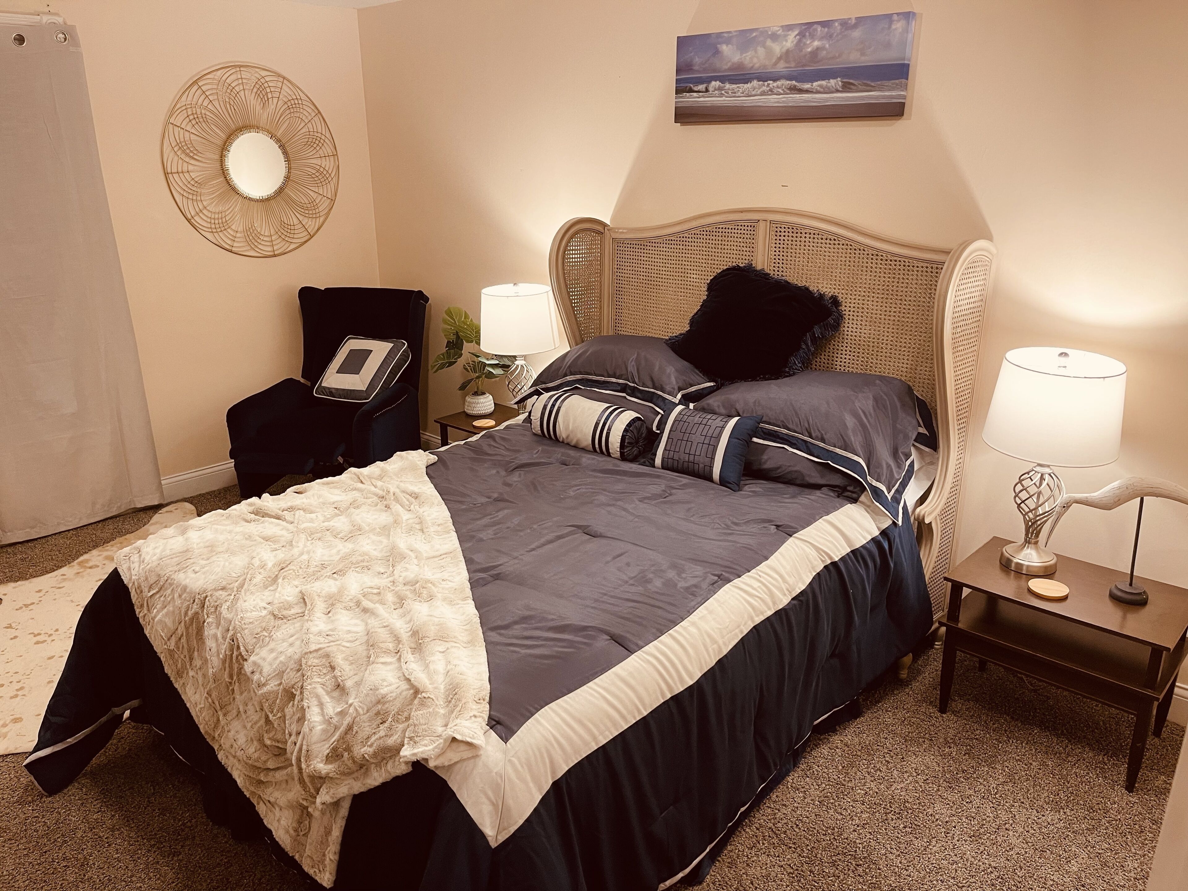 A neatly arranged bedroom with a bed, bedside tables, a lamp, a wall-mounted mirror, and a painting.