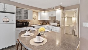 Een moderne keuken met witte kasten, een granieten aanrecht en een centraal eiland met placemats en een bloemenvaas.