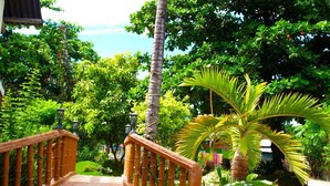 A wooden bridge leading to a lush garden with palm trees and a view of the sea. - Purple Snapper Dive Resort - Hostel/backpacker Accommodation (Daanbantayan)