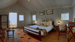 Ein geräumiger Zeltraum mit einem großen Bett, Holzmöbeln und Kunstwerken an den Wänden.