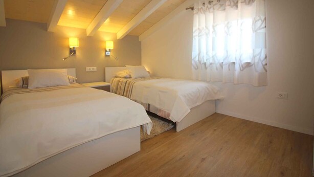 Une chambre avec deux lits, un plancher en bois et une fenêtre avec des rideaux.