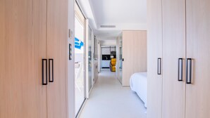 A modern hotel corridor with wooden wardrobes, a visible kitchen area, and a bed in the distance. - 1-Br Apartment, Sea View Terrace & Parking (Cannes)