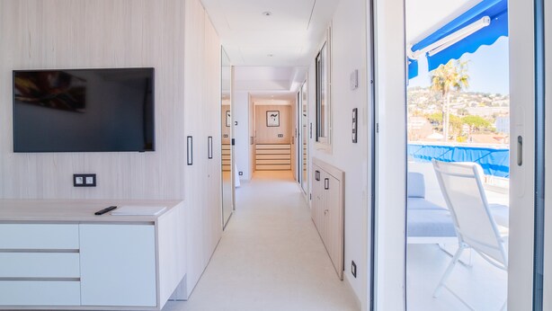 A modern hotel corridor with a flat-screen TV mounted on the wall, a kitchenette area, and a balcony with a view of the landscape. - 1-Br Apartment, Sea View Terrace & Parking (Cannes)