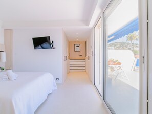 A modern hotel room with a bed, a TV mounted on the wall, and a balcony with a pool view.