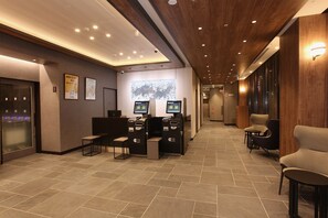 Um lobby moderno com uma receção, dois monitores, um ecrã digital e uma área de estar com cadeiras.