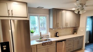 A modern kitchen with stainless steel appliances, a large window, and a ceiling fan. - Door County Cottage, near Haines Beach! (Sturgeon Bay)