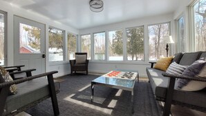 A spacious room with large windows, a central coffee table, a sofa, and a chair. - Door County Cottage, near Haines Beach! (Sturgeon Bay)