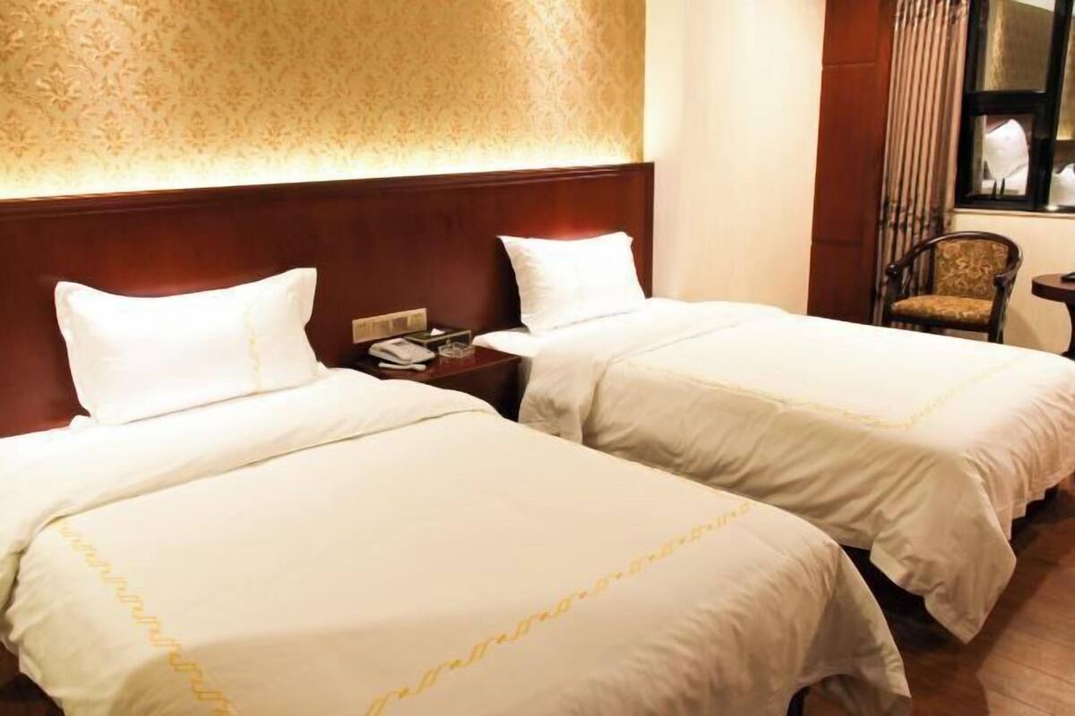 Ein Hotelzimmer mit zwei Betten, einem Holzkopfstück, einem Nachttisch mit Telefon und einem Stuhl am Fenster.