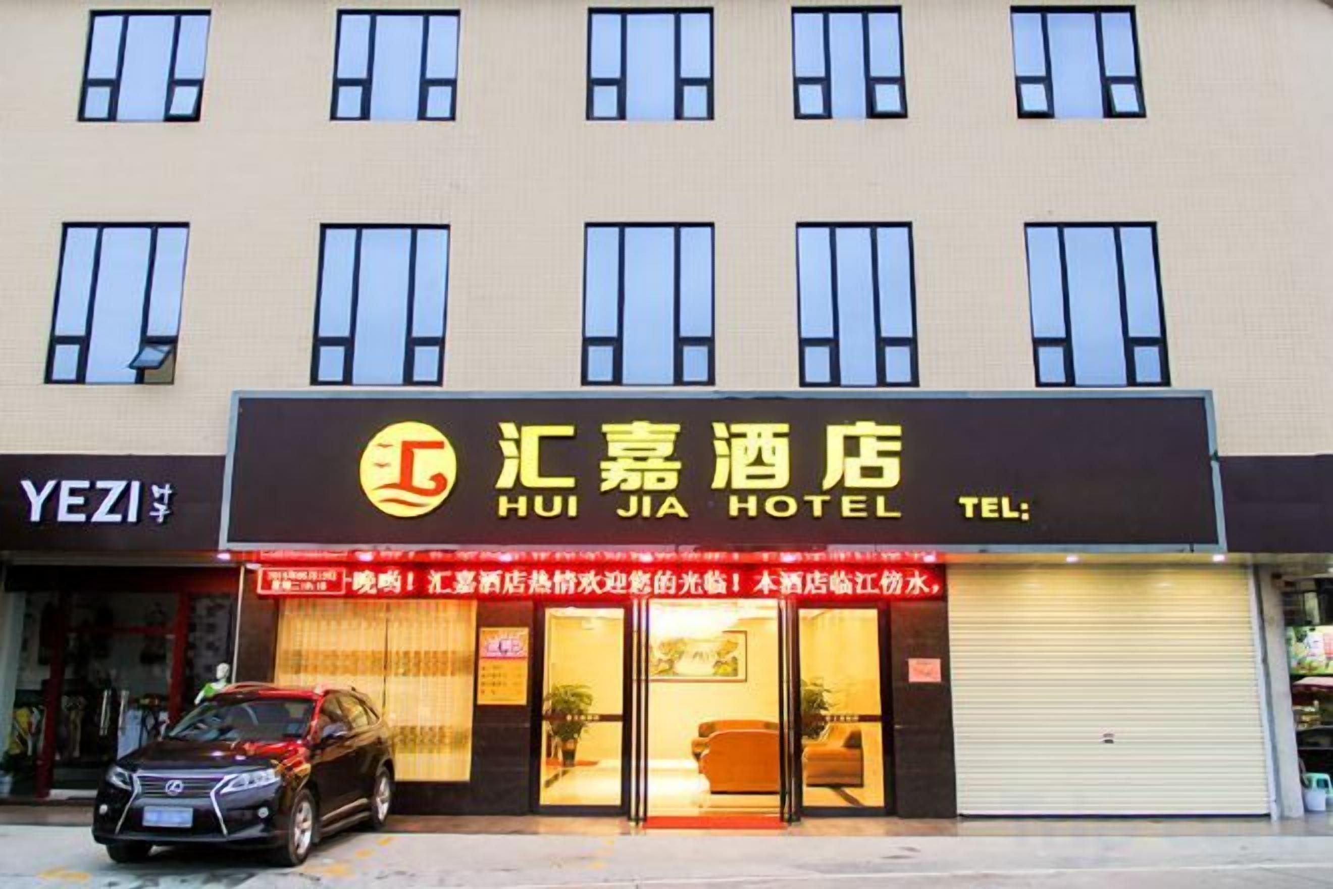 A hotel with a large signboard, a closed shop, and a parked car in front.