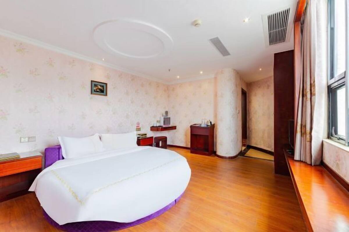 Ein Hotelzimmer mit einem großen Bett, Holzboden, einem Schreibtisch mit Stuhl, einem kleinen Tisch und einem Fenster mit Vorhängen.