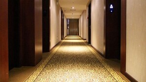 Pasillo de hotel con alfombra estampada, puertas de madera y techo iluminado.