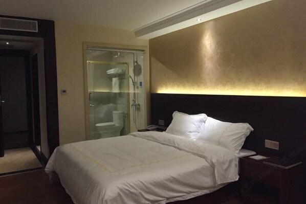 A hotel room with a bed, a nightstand, a glass-enclosed shower, and a wall with a textured finish. - Vica Hotel (Huazhou)